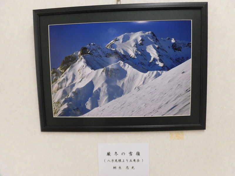 「厳冬の雪嶺」というタイトルが付けられた、青い空の下で雪をかぶった雄大な山々を写した写真作品を、額縁に入れて壁に飾った写真