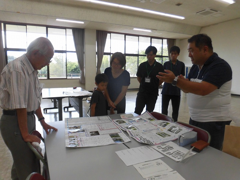 数人の大人が子供を交え、机の上に広げられた資料を囲んで熱心に話を聞いている様子の写真