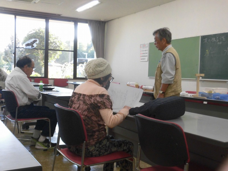 室内で、木村晴生先生が立って講師のように話し、複数の参加者が椅子に座り机に向かっている、講習会の様子の写真