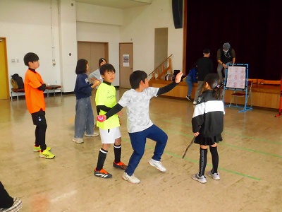 広間の中で子どもたちが集まり、棒やボールを持って遊んでいる様子を写した写真