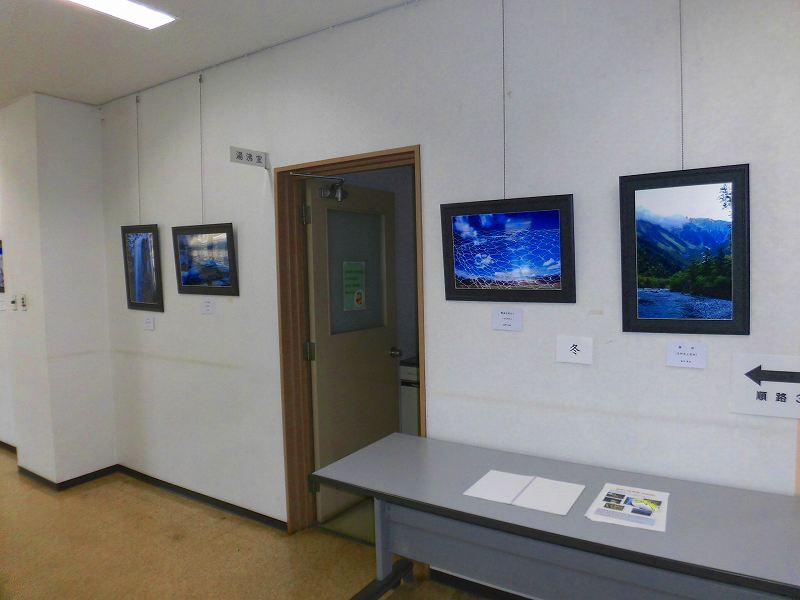 屋内の白い壁に季節をテーマにした写真が展示されており、滝や山、雪景色など自然を写した作品が並んでいる写真展の様子の写真