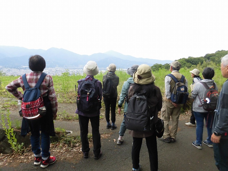 リュックを背負った男女のグループが、遠くに山々を望む開けた場所で景色を眺めている様子を捉えた写真