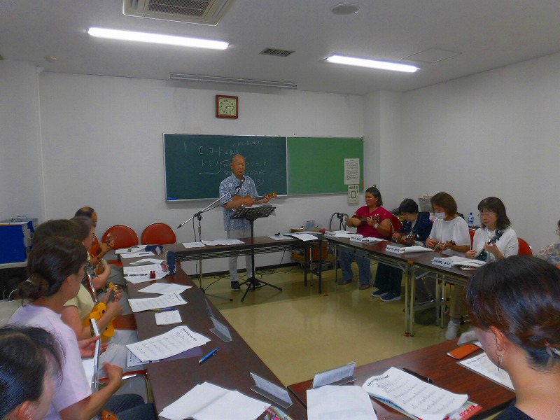 鈴野友市さんがウクレレを弾きながら指導しており、複数の受講者が真剣な表情でウクレレを練習している教室風景の写真