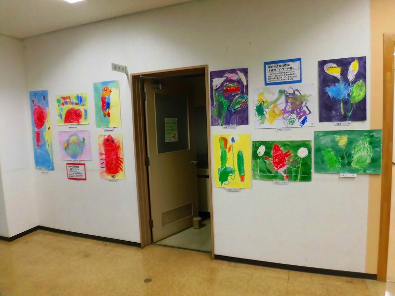 廊下の壁に、子どもたちが描いた色とりどりの絵が多数展示されている様子を写した、子どもの作品展示の写真