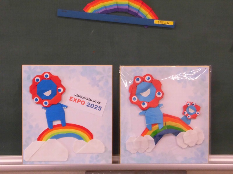 折り紙で作られた大阪・関西万博の公式キャラクター「ミャクミャク」の作品が2枚並べて展示されている写真
