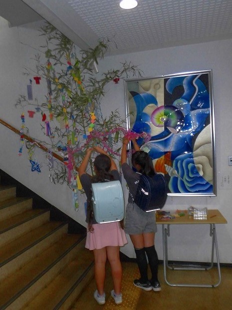 二人の子どもが笹に短冊や飾りをつけて七夕の準備をしている様子を写した、七夕飾りの写真