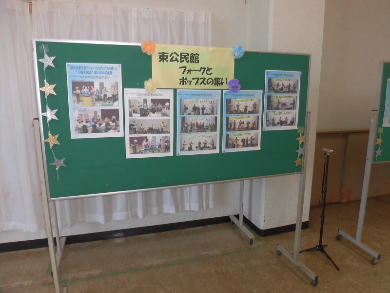 緑色の掲示板に「東公民館 フォークとポップスの集い」という掲示がされ、イベントの様子を撮影した写真が複数枚貼り付けられている展示ボードの写真