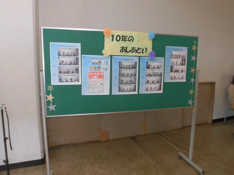緑色の掲示板に「10年の あしあと」と書かれた装飾が施され、イベントの様子を捉えた写真が複数枚貼り付けられている掲示板の写真