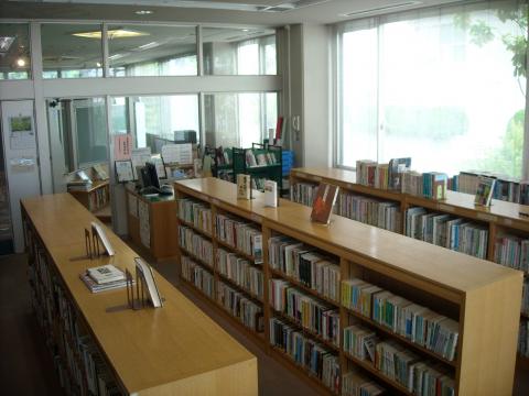 背の低い木製の書架が複数並べられており、多くの書籍が整然と並べられている、窓から明るい光が差し込む図書館の内部を撮影した写真