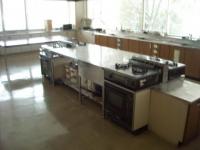 白い調理台と複数のコンロが設置されたステンレス製の作業台が中央に配置されている、広々とした調理室を写した写真