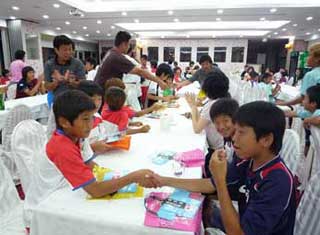 白いクロスがかけられたテーブルを囲み、大勢の子供たちが着席し、中央では赤と紺のユニフォームを着た少年二人が握手をしていたり、楽しそうに談笑している交流会の様子の写真