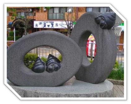 正面と斜めに設置された中心に穴が空いた二つの大きな石の輪に、ヤドカリを思わせる黒い石のオブジェが配置された抽象的な屋外彫刻の写真