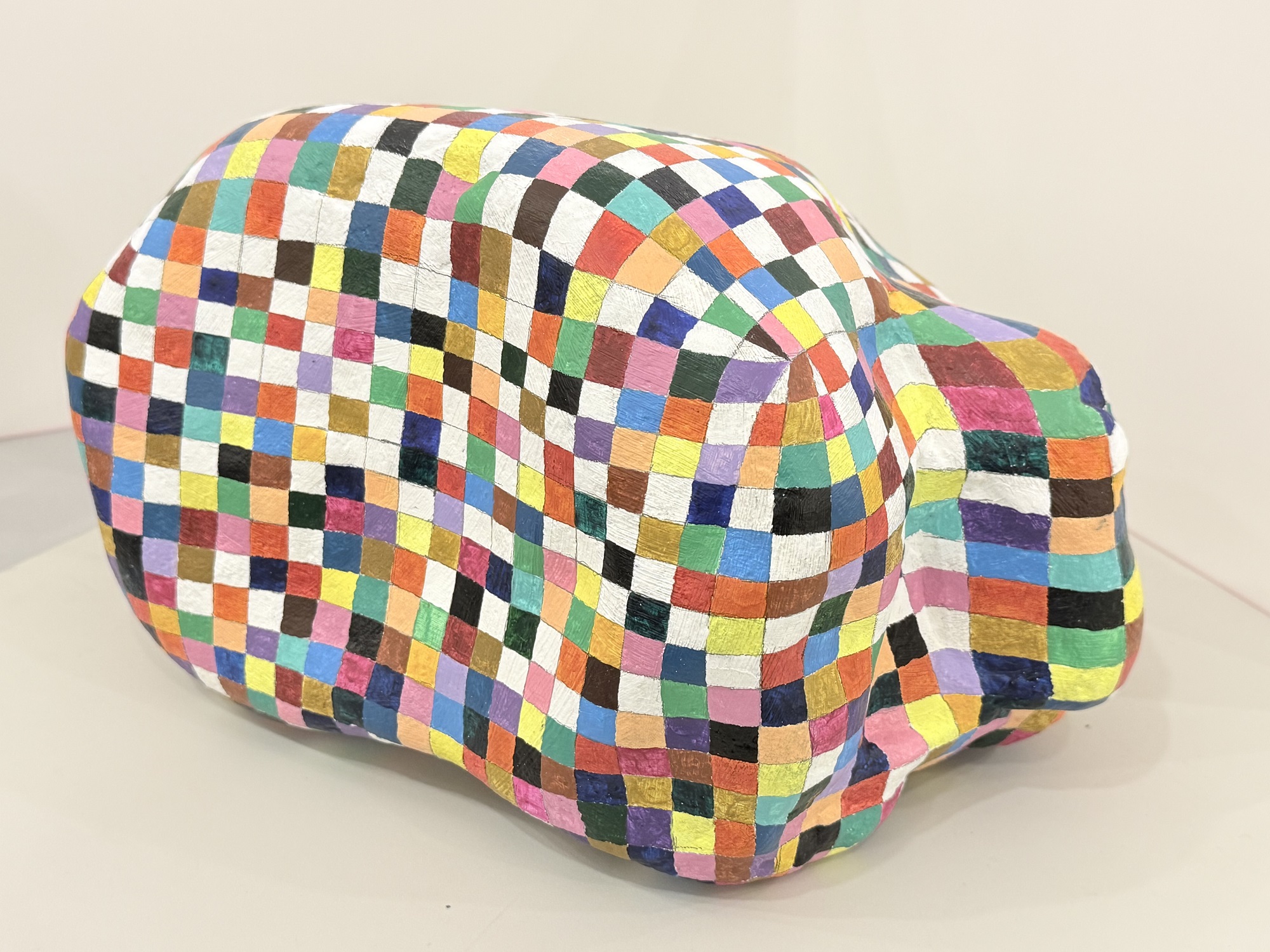 全体的に丸みを帯びた抽象的な形の表面に、赤、青、黄色などの色鮮やかな正方形がモザイク模様に描かれた作品の写真