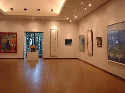 部屋の奥には窓があり木々が見えており、壁には様々な大きさや様式の絵画が等間隔に展示された広々とした市民ギャラリーの様子を写した写真