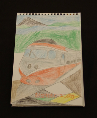 スケッチブックに遠くの富士山や湖を背景に、赤や灰色で塗られたロマンスカーのイラストを大きく描いた写真