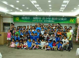 「坡州市・秦野市 青少年親善交流会」と書かれた横断幕の下で、多くの大人や子供たちが混ざり合い、集合している交流会の写真