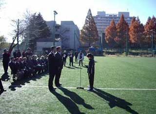 人工芝の屋外グラウンドで、多くの関係者が見守る中、選手が選手宣誓を行っている様子の写真