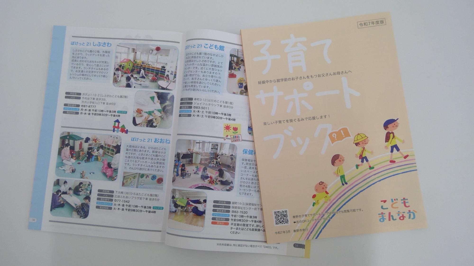 薄いオレンジ色の表紙に「子育てサポートブック 令和7年度版」と書かれ、虹色の道の上を子供たちが歩いているイラストが描かれた冊子が、左側に開かれた状態の別の子育て支援施設を紹介するページがある冊子に重ねられている写真