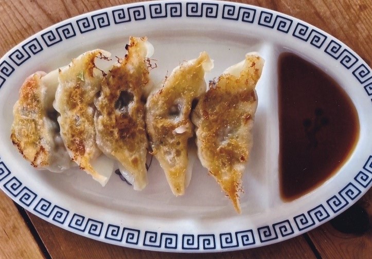 楕円形の皿に餃子のたれと、焼き目のついた餃子が並べられた写真