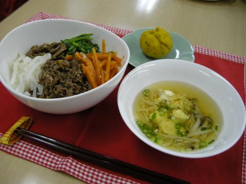 牛肉のそぼろ、千切り玉ねぎ、人参、ほうれん草のナムルが白ご飯の上にきれいに盛り付けられた丼と、きのこや卵の入った中華スープ、小さな皿に黄色い丸いデザートが添えられた写真