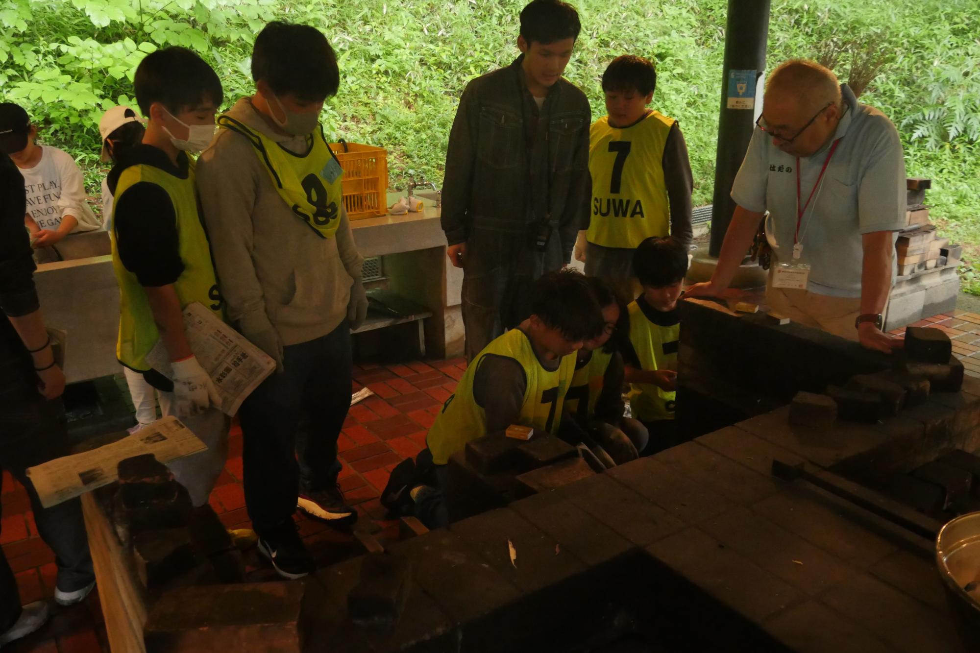 複数の子供たちがかまどをのぞき込んでおり、大人がその様子を見守っている様子の写真