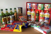 奥にはお茶のペットボトルや缶コーヒー、箱入りの調味料セット、中央にはパスタ、缶詰、レトルトカレー、オリーブオイル、手前にはインスタント食品が並べられている、集まったフードドライブの持ち寄り食品の写真