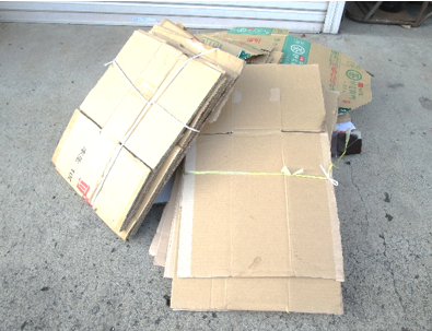 何枚もの段ボールが畳まれ、紐で十字に結ばれて積み重ねられている様子を写した写真