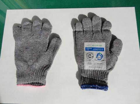 平らな台の上にグレーの軍手が2つ並んで置かれ、左側の軍手の手首部分にピンク色の縁取りがあり、青い縁取りの右側の軍手には「資源循環型商品 よみがえり」というリサイクルマークが印刷されたラベルが貼られている写真