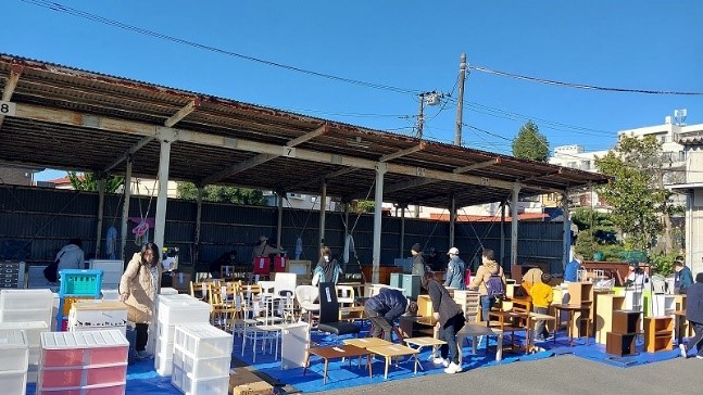 イベント会場に並べられたリユース品の椅子やプラスチックケースなどを、多くの人々が品定めをしている様子を写した写真
