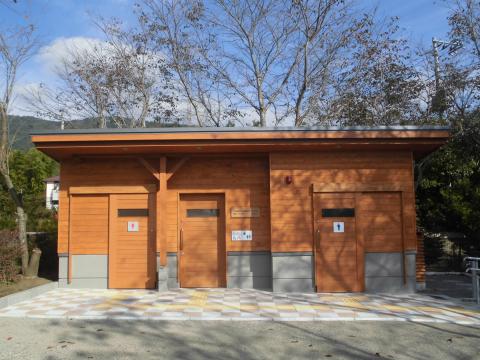 木材の壁と灰色の土台を持つ、男女別と多目的の扉が並ぶきれいな公衆トイレの建物を正面から捉えた写真