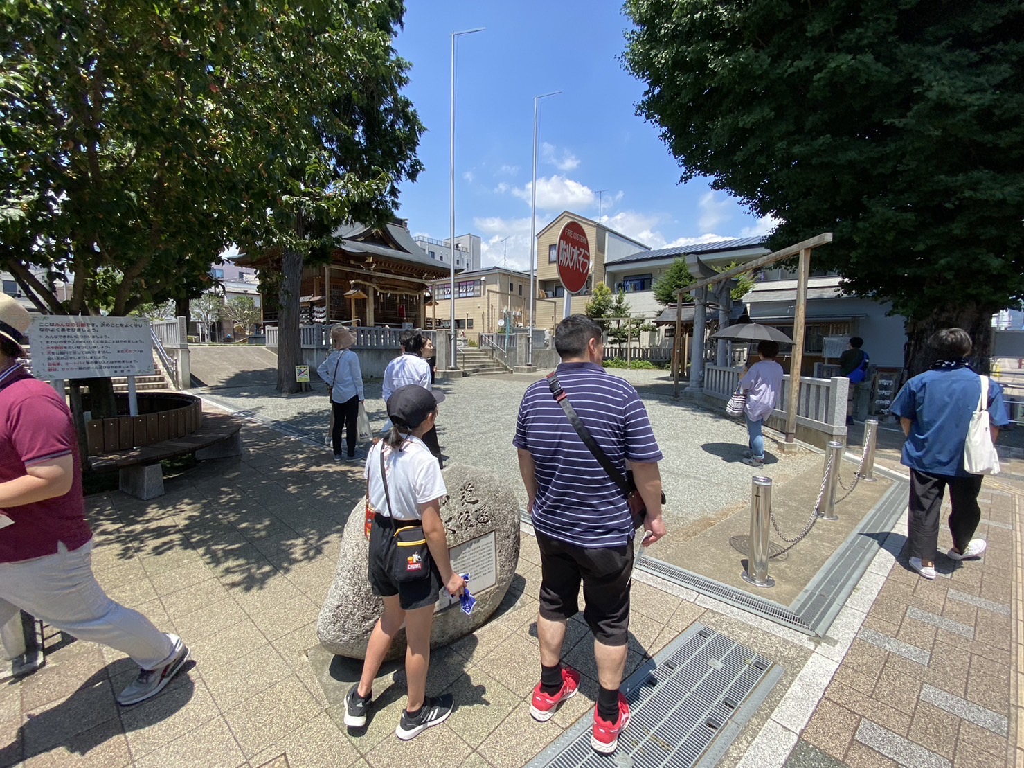 渋沢駅の一角に設置された神社の境内で数人の人々が参拝や見学をしている様子を捉えた写真