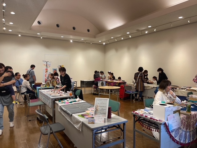 木張りの床と白い壁の広々とした屋内のスペースに、複数のワークショップのテーブルが並び訪れた人々で賑わっている様子の写真