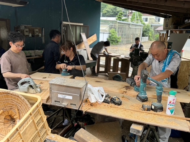 屋外の作業場で地域の人々が電動工具を使って木材を加工している様子の写真