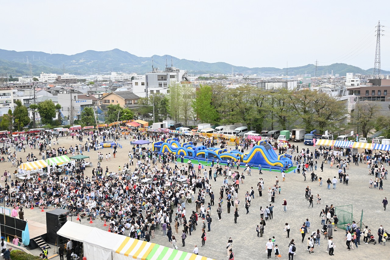 大勢の来場者が集まり、中央には青と黄色の巨大なエア遊具、周囲には様々な出店テントやステージなどが設けられた広大な広場で行われているイベントの俯瞰写真
