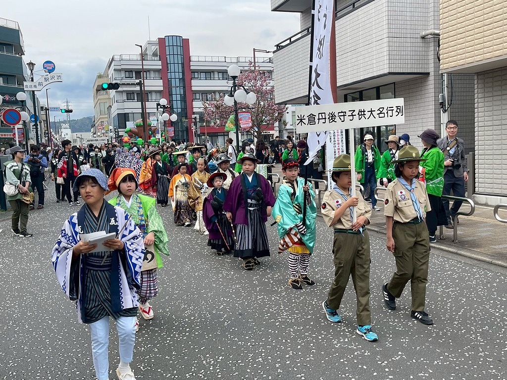 カラフルな着物や裃などの時代衣装に身を包んだ子どもたちが練り歩き、その先頭をプラカードを持ったボーイスカウトらしき制服姿の少年たちが歩いているパレードの写真