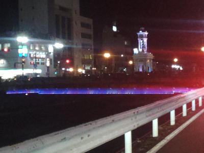 上部がピンク色にライトアップされた夜の街中の時計台の写真