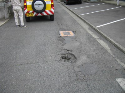 道路の一部がひび割れ、舗装が剥がれ落ちて大きな穴ぼこを示す写真