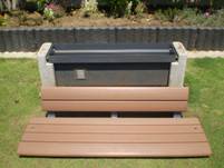 芝生の上に設置されているベンチの茶色の木製の座面が前にスライドし、災害時の緊急グッズが収納できるベンチの写真