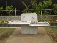 複数の蛇口と飲み口がついており、手洗い場や水飲み場として利用可能で、左右に長い水受けがあるコンクリート製の水道設備の写真