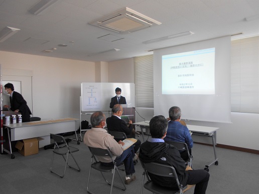 会議室で椅子に座った4人の男性がスクリーンの資料を見ている説明会の様子の写真