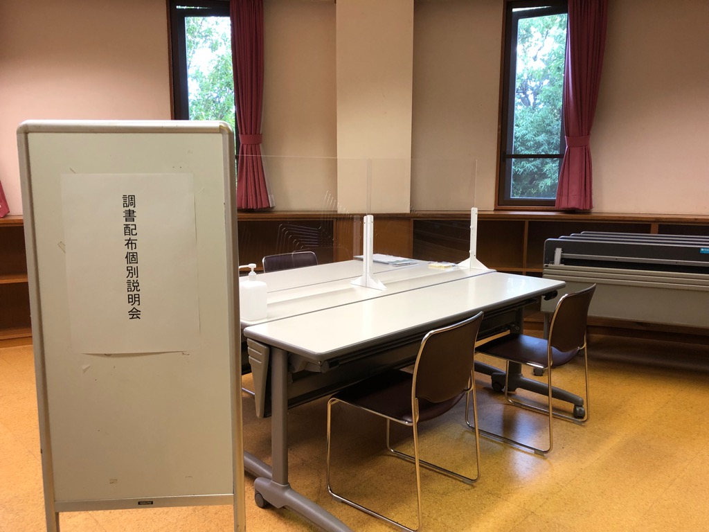 白い立て看板の後ろにテーブルとイスが設置された部屋の写真