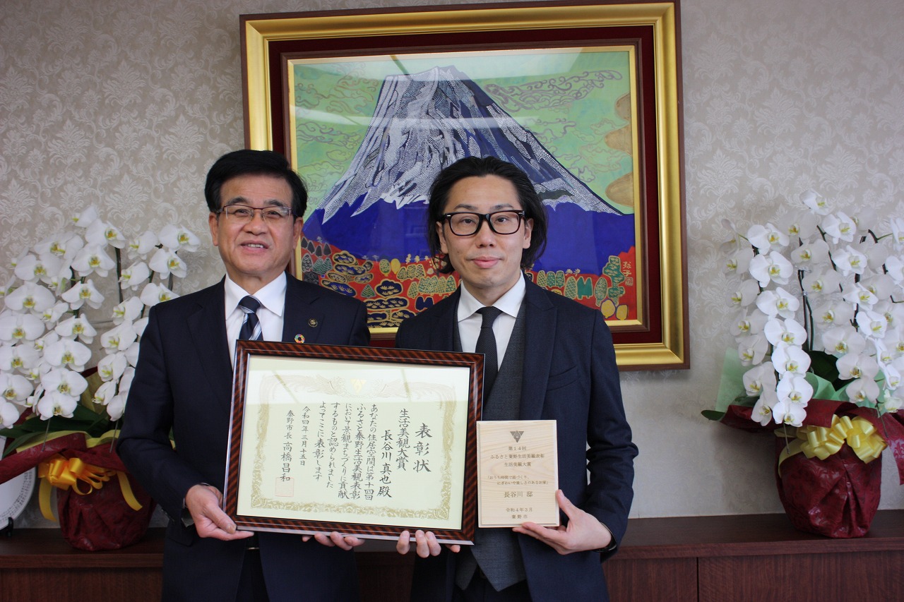 高橋市長と男性が額縁入りの表彰状を一緒に持ちカメラに向かって笑顔で立っている記念写真