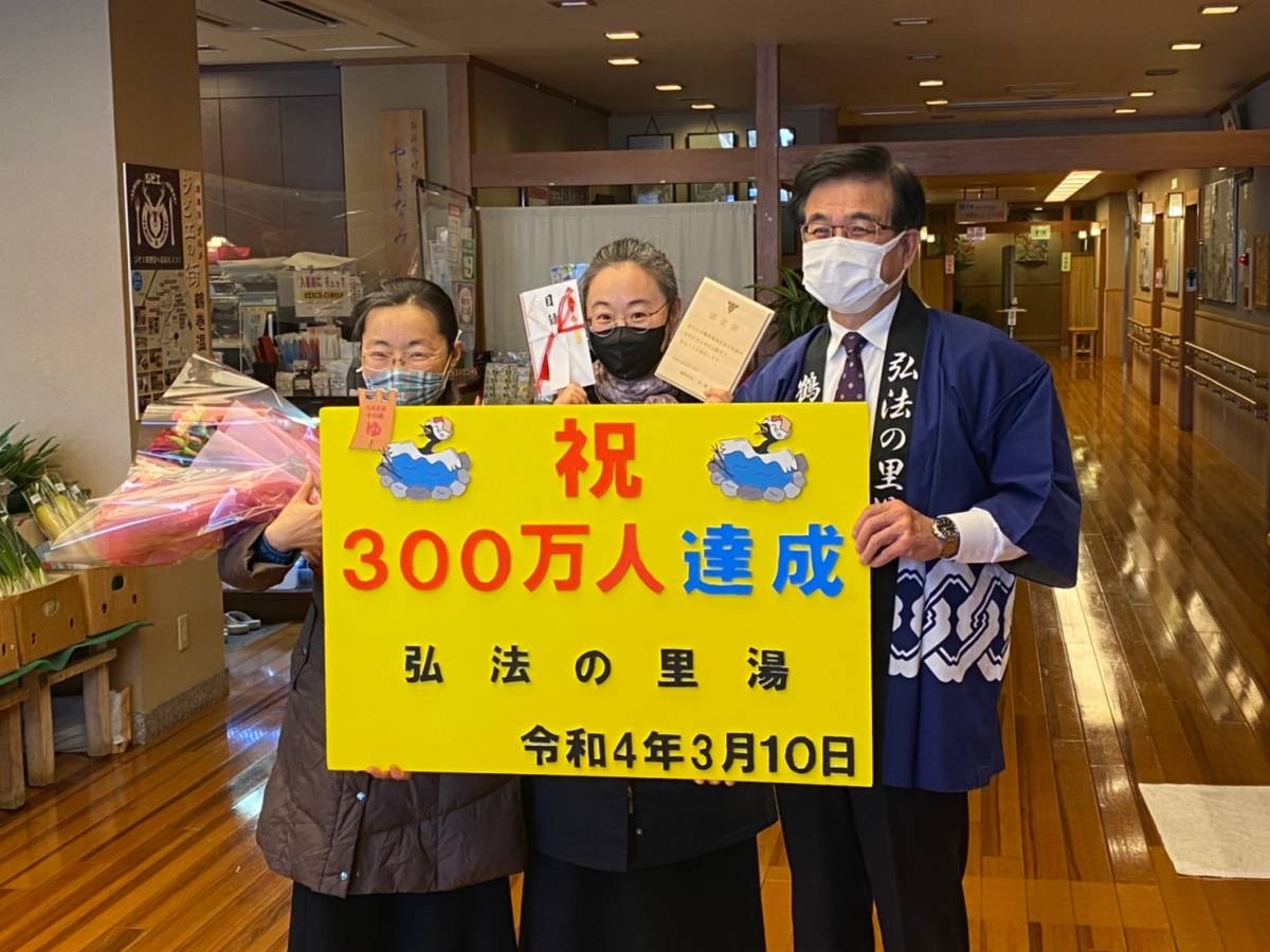 祝300万人達成の黄色い看板を中央に、法被を着た高橋市長と、花束や目録を持った女性2名が一緒に記念撮影を行っている写真