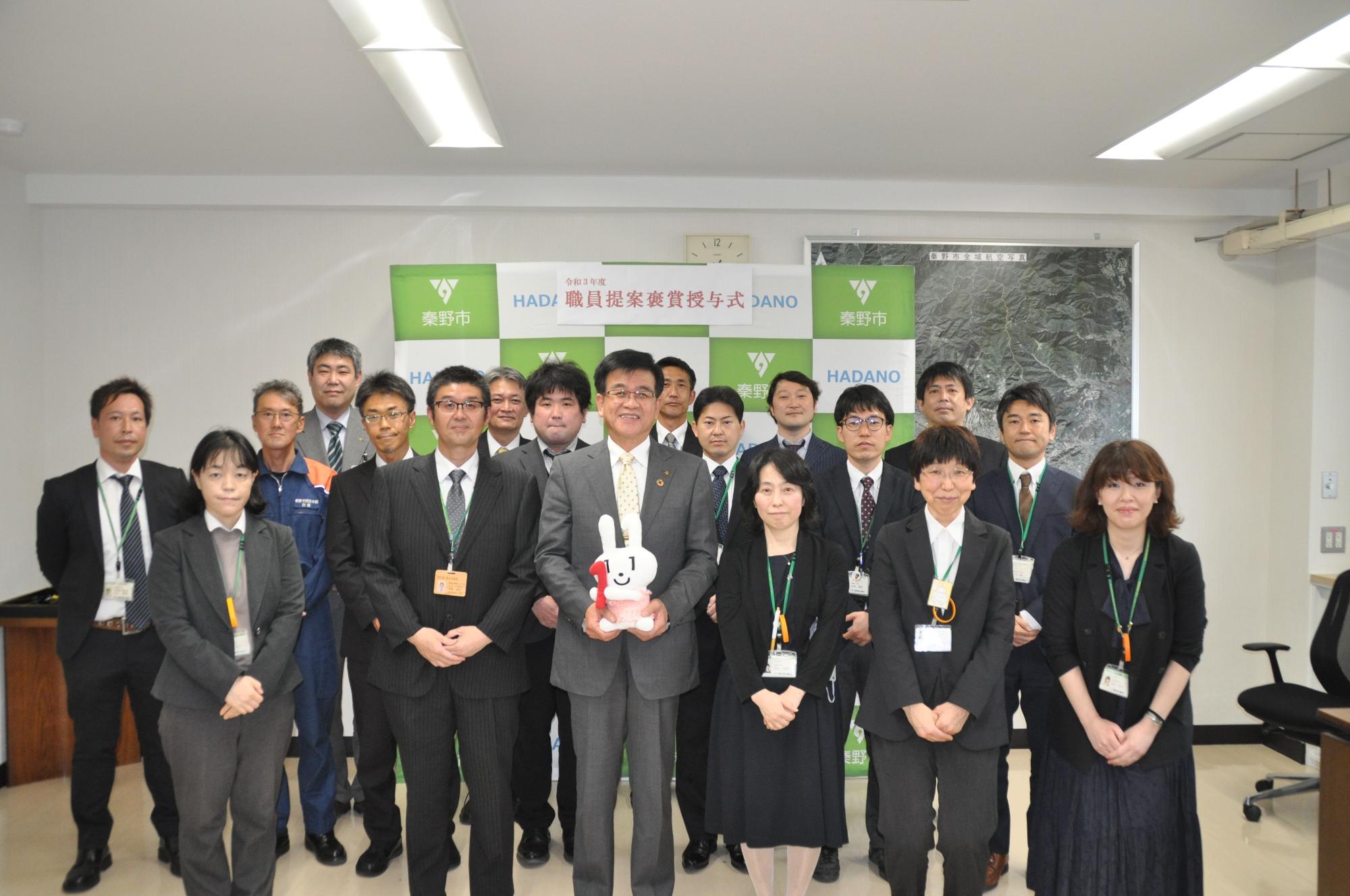 マイナちゃん人形を持った高橋市長を中心にたくさんの男女が並んで撮影した集合写真