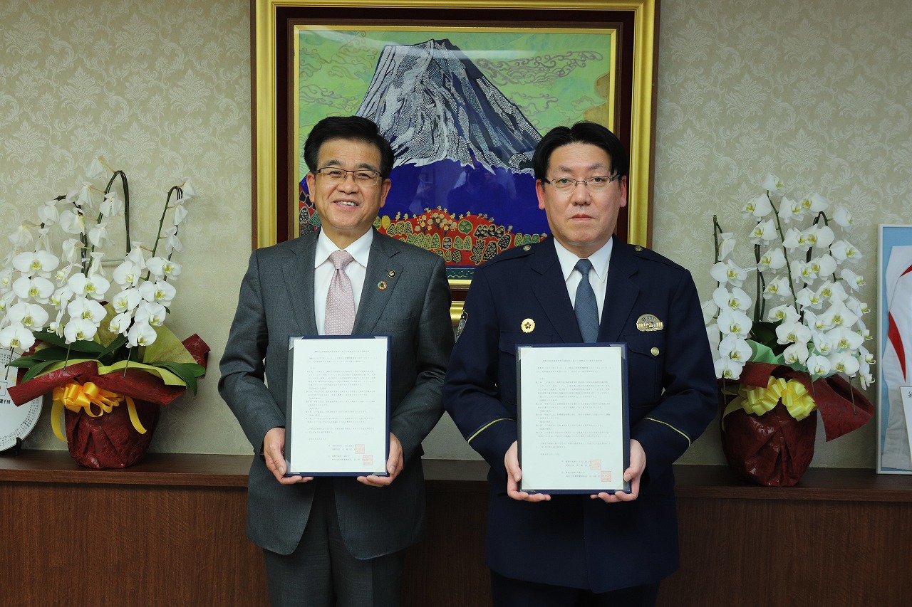 高橋市長と警察官の制服を着た男性が、それぞれ両手で協定書を持って並んで写っている記念写真