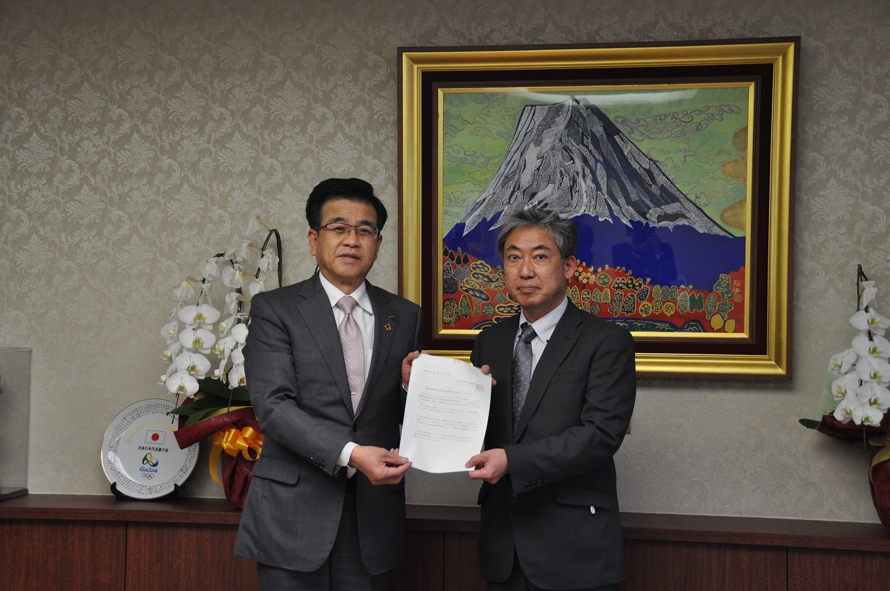 高橋市長と伊藤会長が中央で1枚の紙を一緒に持ち、カメラに向かって並んで立っている様子を捉えた写真