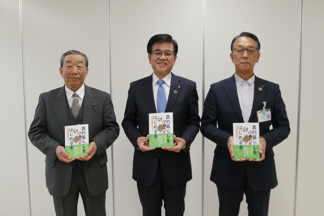 高橋市長の両側に2名の男性が立ち、それぞれ「農的暮らしをはじめる本」というタイトルの本を持って並んでいる写真