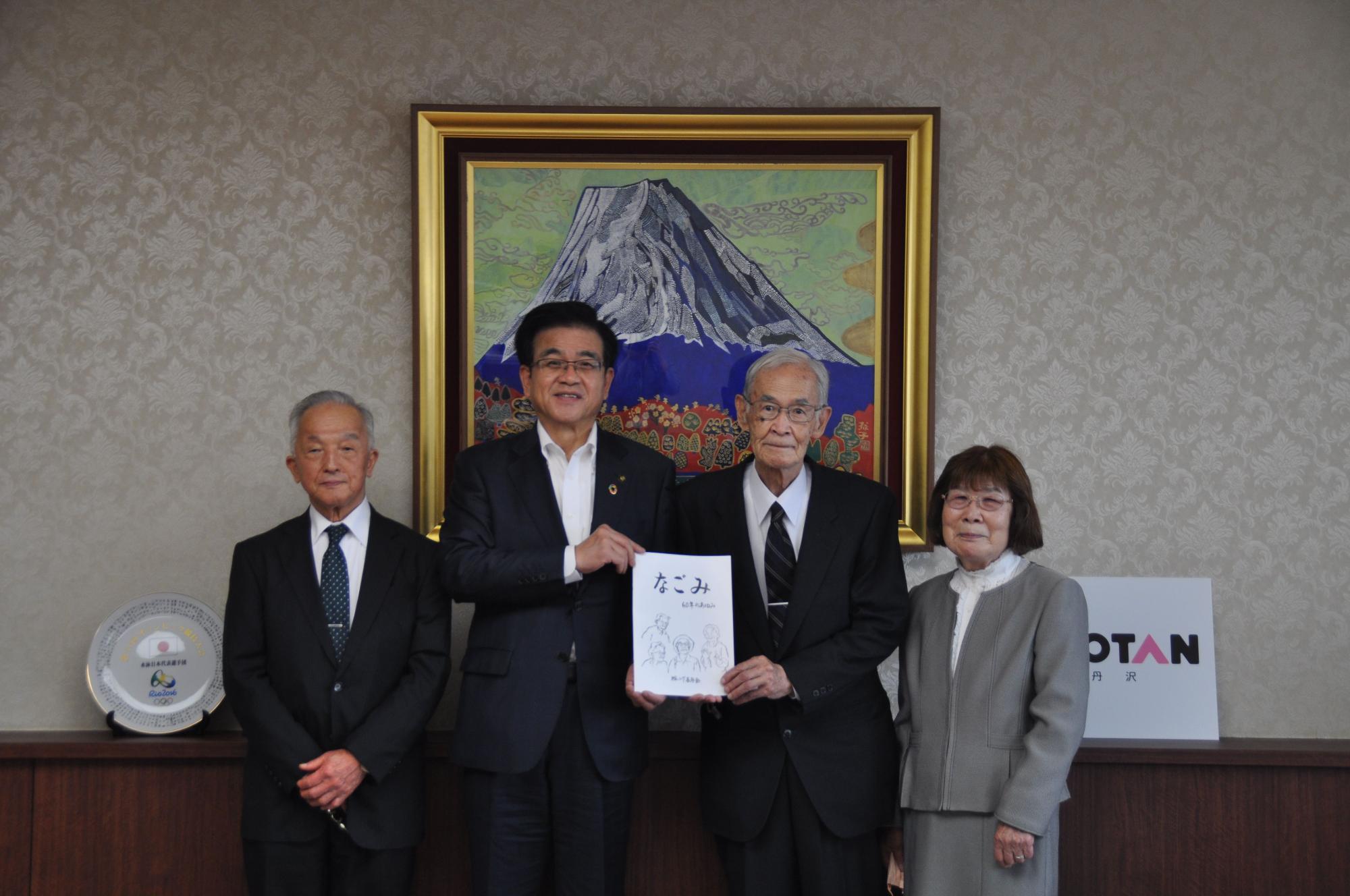 中央の高橋市長と年配の男性が「なごみ」と書かれた冊子を手に持ち、2人の両側に年配の男性と女性が立ち記念撮影をしている写真