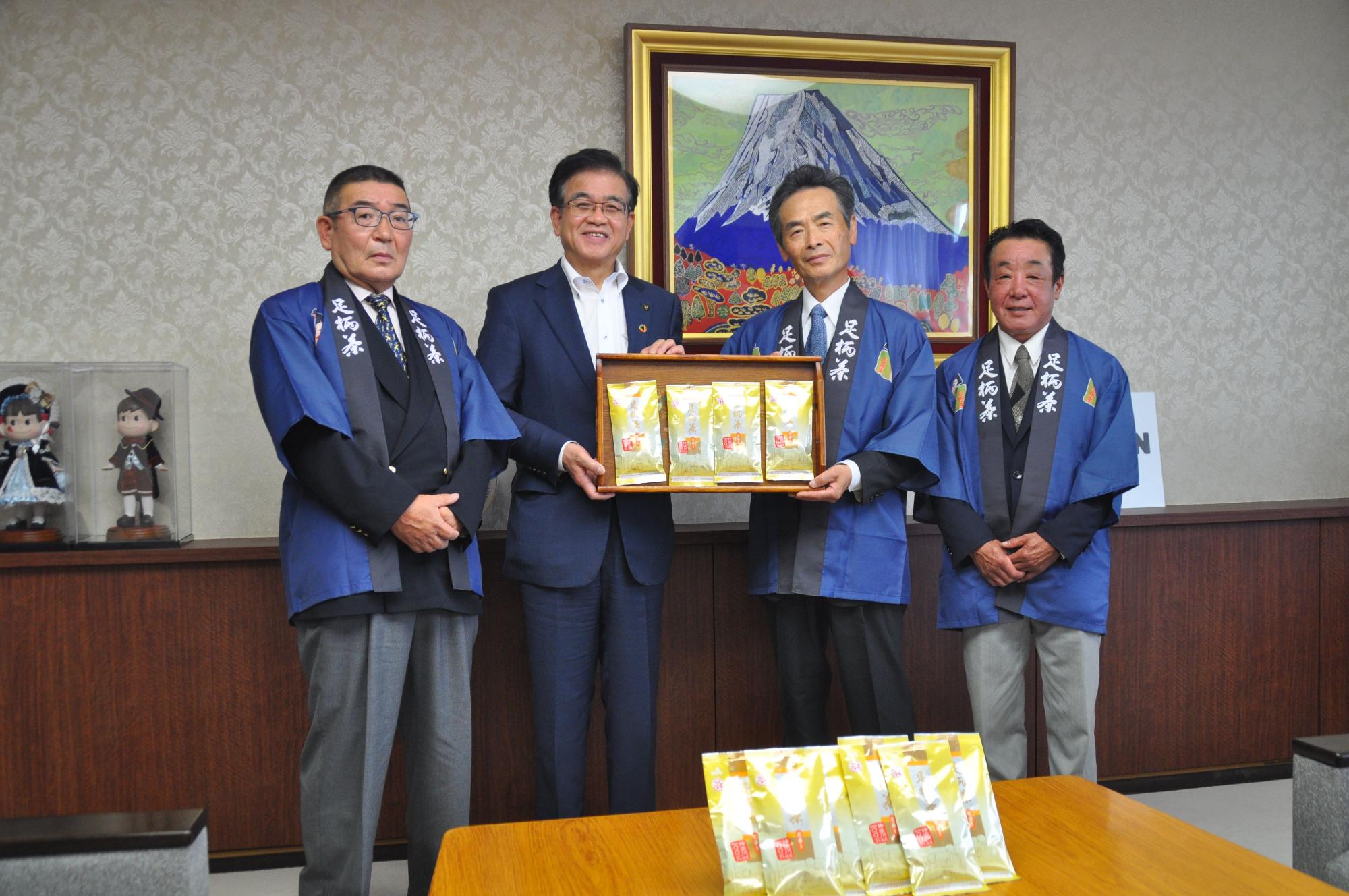 高橋市長と「足柄茶」と書かれた法被を着た3名の男性が、足柄茶のパックが載ったトレーを持って記念撮影を行っている写真