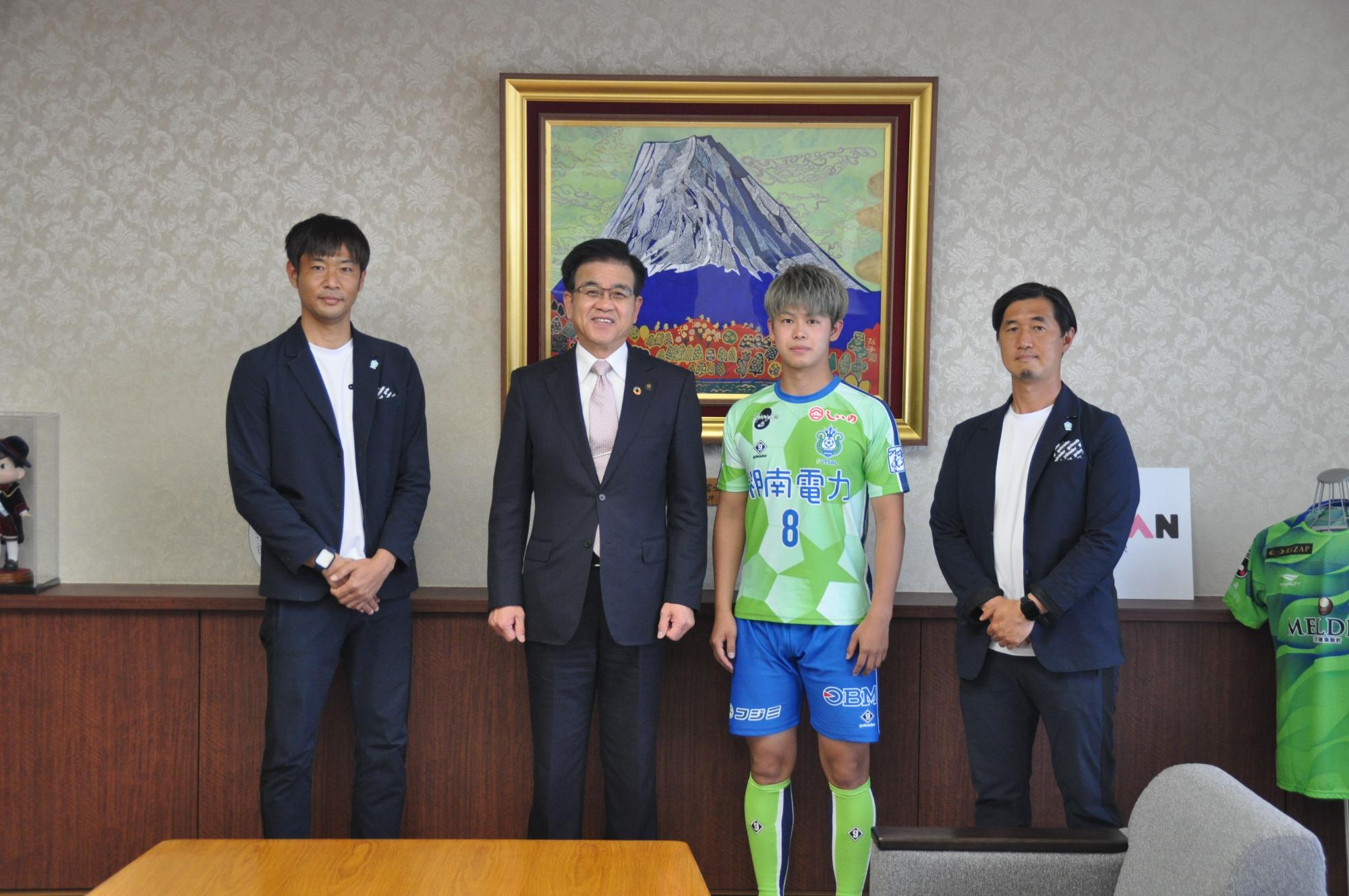 佐藤代表取締役と背番号8のユニフォームを着用した薮内選手、関係者の男性と高橋市長が並んで記念撮影をしている写真